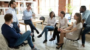 A mixed gender group of business people sitting in a circle and laughing.