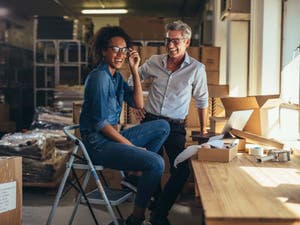 A man and woman business owner wearing glasses at a workbench in a workshop