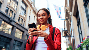 A woman walking outside, taking off her headphones and using her mobile phone