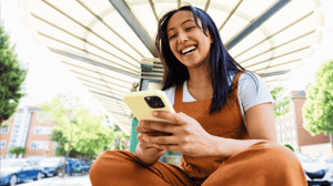 A woman sits outside using her mobile device