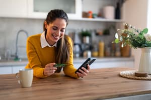 A woman smiling while looking at her card and mobile phone