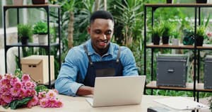 Joyful entrepreneur sitting in a flower shop making an ACH transfer.
