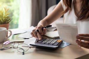 A woman uses a calculator while holding a bill