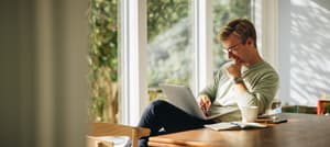 Smiling man browsing on laptop at dining table