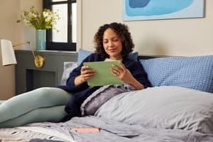 Woman looks at tablet while sitting on bed