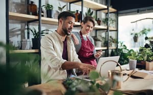 Two small business owners behind store counter setting up account on laptop