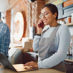 Woman on the phone behind a counter using a laptop