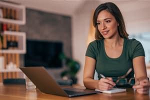 A woman in front of a laptop taking notes about her credit score and how to improve it