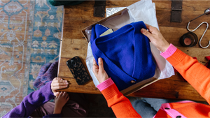 A person unboxing a blue sweater from a box.