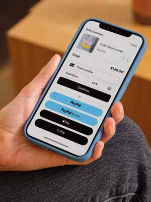 Person holding mobile phone showing checkout screen with payment options including debit/credit card, PayPal, Pay Later, and Apple Pay