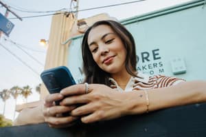 Mujer sonriente usando su teléfono al aire libre. 