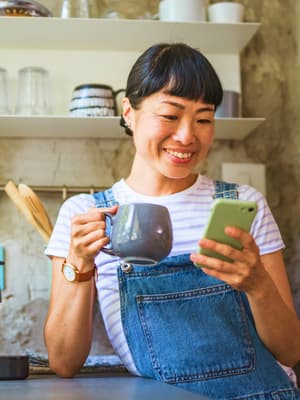 Woman in overalls enjoying a cup of coffee while holding a phone