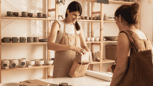 Pottery shop owner packing a handmade ceramic product into a paper bag for a customer.