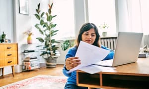 A woman sitting on the ground near a coffee table reviewing her bank statement.
